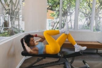 A woman in a yellow and blue fitness outfit performs a single leg extension exercise.