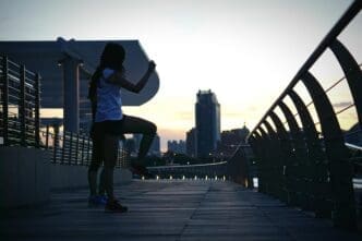 Two women are exercising on a footbridge, silhouetted against a bright sky.
