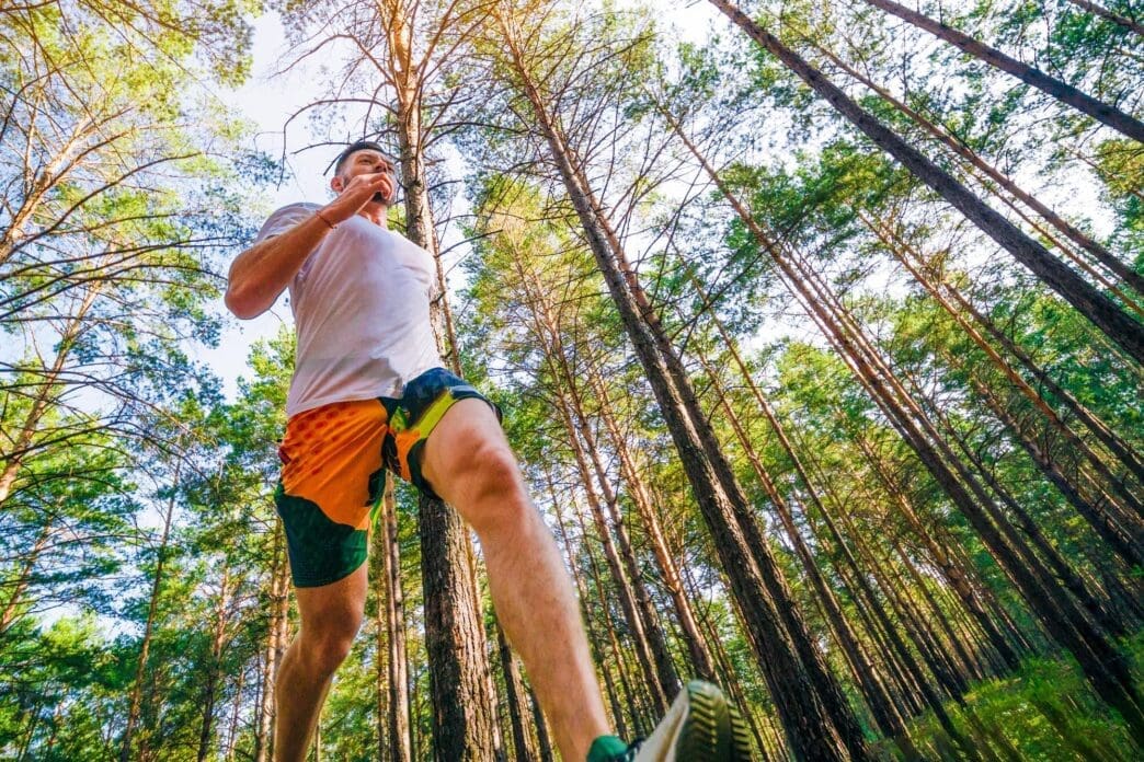 A young man in athletic wear jogs through a park.