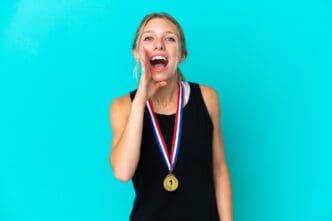 Young woman with fair skin wearing medals, isolated against a blue backdrop, shouts with her mouth open.