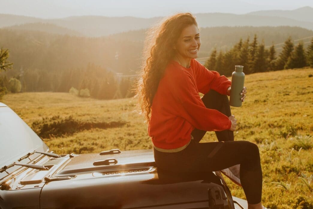 Young woman smiles while reclining on the hood of an all-terrain vehicle in a rural setting.