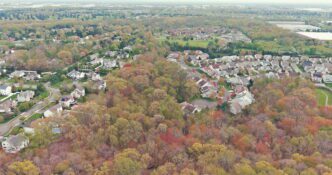 Aerial view of closely packed apartment buildings in a suburban area, with a small town visible in the distance.