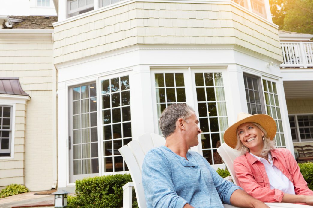 A mature couple sits in a backyard, laughing and conversing while enjoying a summer day.