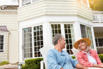 A mature couple sits in a backyard, laughing and conversing while enjoying a summer day.