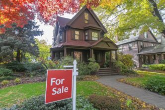 Bright red "For Sale" sign in front of a charming suburban home with fall foliage.