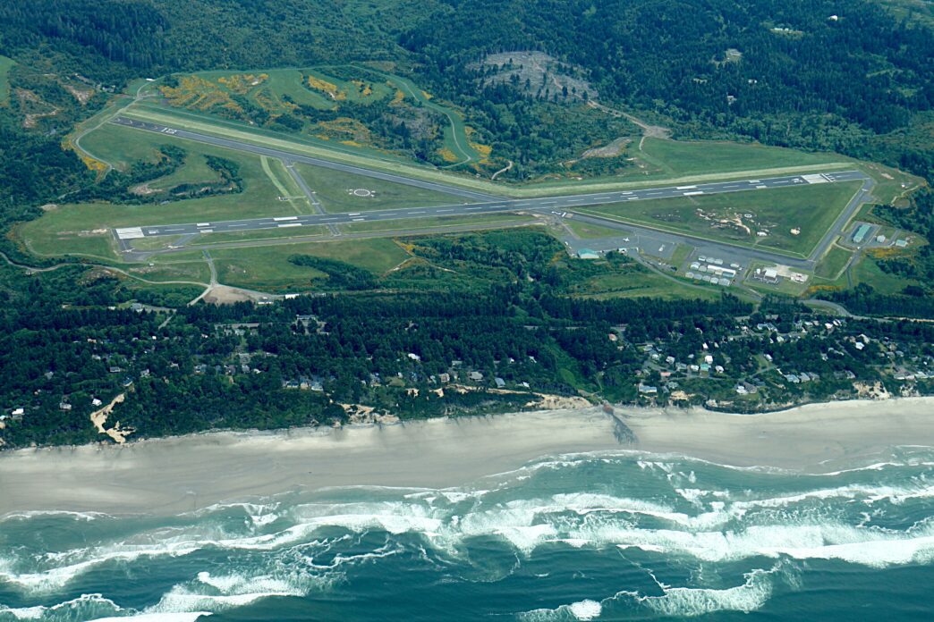 Aerial view of Newport Municipal Airport in Oregon, situated between dense forest and the coastline.