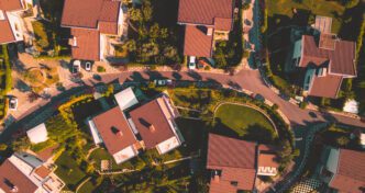 High-angle aerial view of a residential neighborhood with houses featuring terracotta roofs and lush green yards.