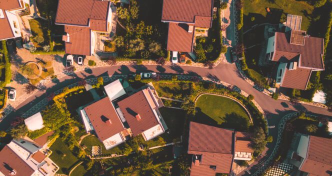 High-angle aerial view of a residential neighborhood with houses featuring terracotta roofs and lush green yards.