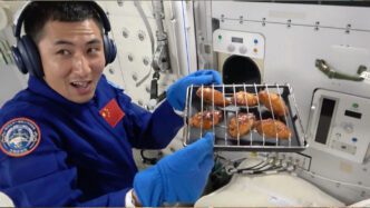 Chinese astronaut in space station holding a tray of baked chicken wings with a cheerful expression.