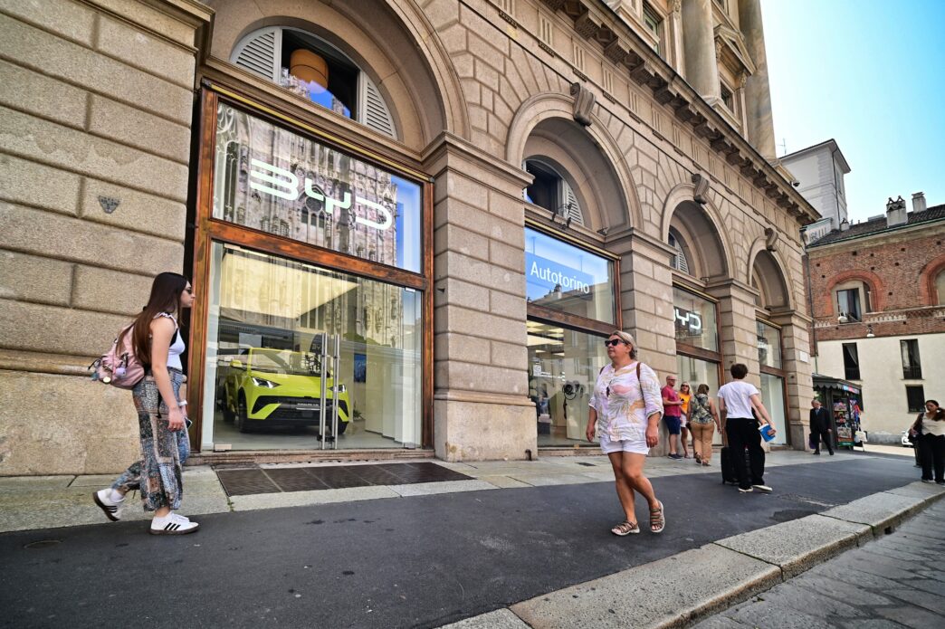 Exterior of the BYD car showroom in Milan, Italy, with a green electric car visible through the window.