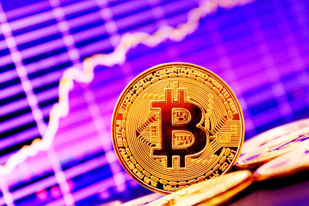 Close-up of a golden Bitcoin coin against a vibrant purple and pink upward-trending line graph.