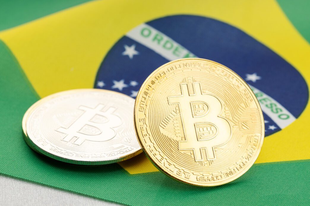 A gold and a silver Bitcoin coin resting on the green, yellow, and blue Brazilian national flag.