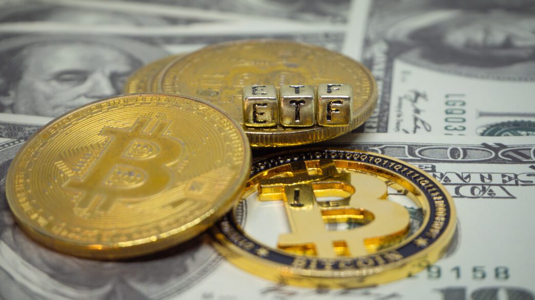 Physical Bitcoin coins and letter blocks spelling "ETF" resting on US dollar bills.