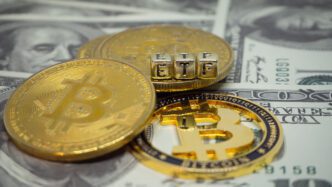 Physical Bitcoin coins and letter blocks spelling "ETF" resting on US dollar bills.