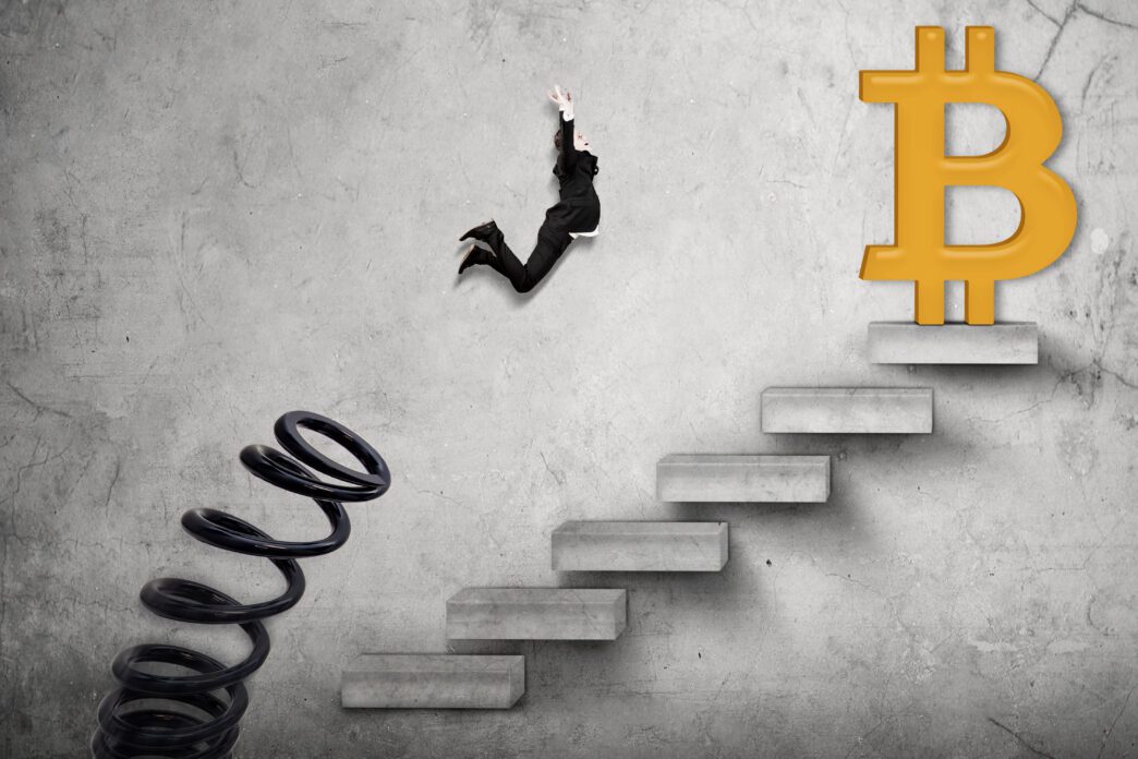 Businessman jumping from a large spring toward a Bitcoin symbol atop a flight of stairs.