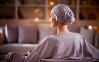 Rear view of a brave woman with cancer wearing a light purple head scarf in a soft-lit room.
