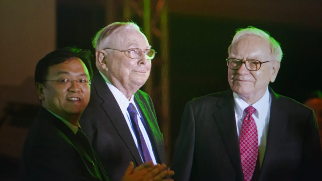 Warren Buffett and Charlie Munger stand with a third man at the Berkshire Hathaway meeting.