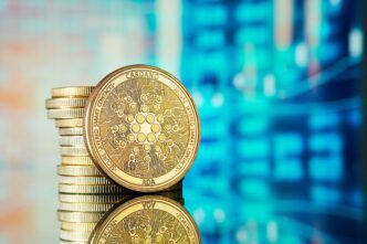 A prominent gold Cardano (ADA) cryptocurrency coin leaning against a stack of similar coins.