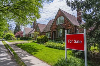 Red "For Sale" sign in the yard of a charming red brick suburban house with lush green landscaping.