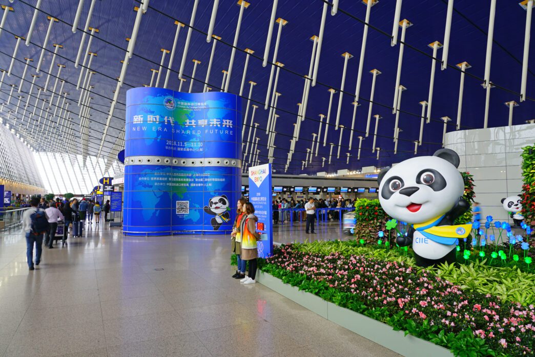 Interior of Shanghai Pudong Airport with CIIE advertisement and large panda mascot statue.