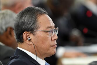 Profile close-up of Chinese Premier Li Qiang wearing glasses and an earpiece.
