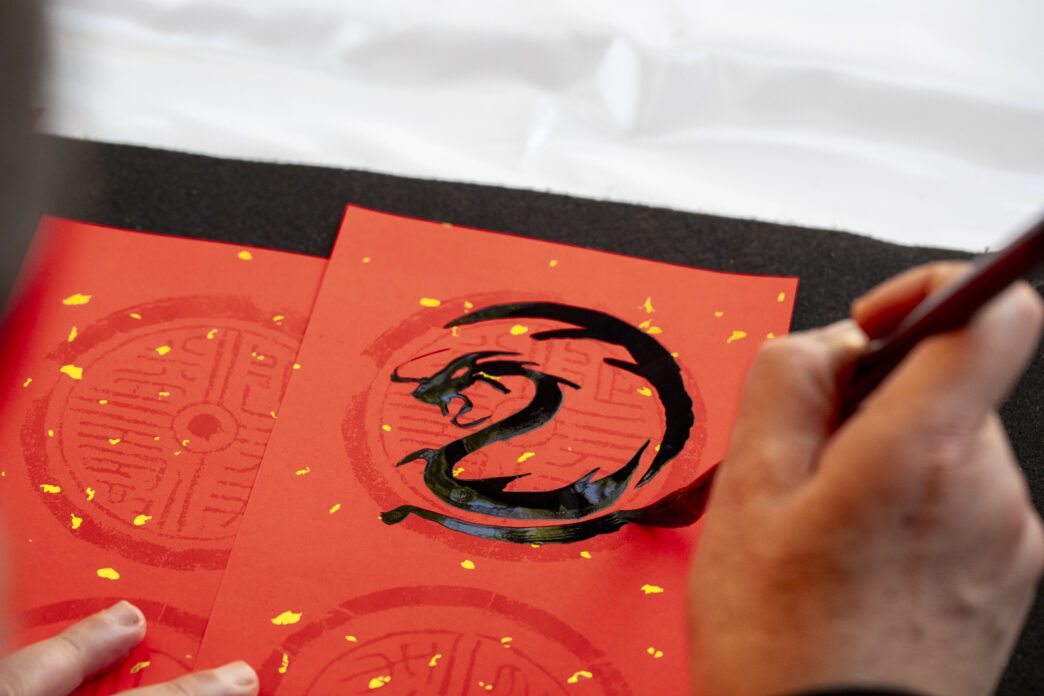 A hand painting a black dragon calligraphy symbol on red paper, celebrating the Chinese Zodiac.