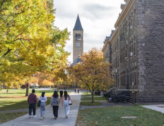 Students walk on the Cornell University campus with the McGraw Clock Tower visible in autumn.