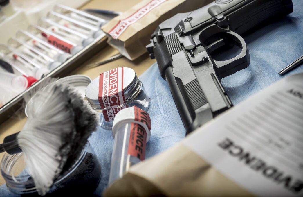 Forensic evidence table with a handgun, test tubes, and fingerprint powder next to evidence bags.