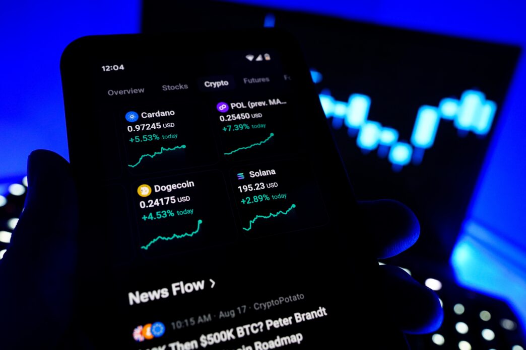 Smartphone displaying crypto market gains for Cardano, Dogecoin, Solana, and Polygon (POL) against a blue background.