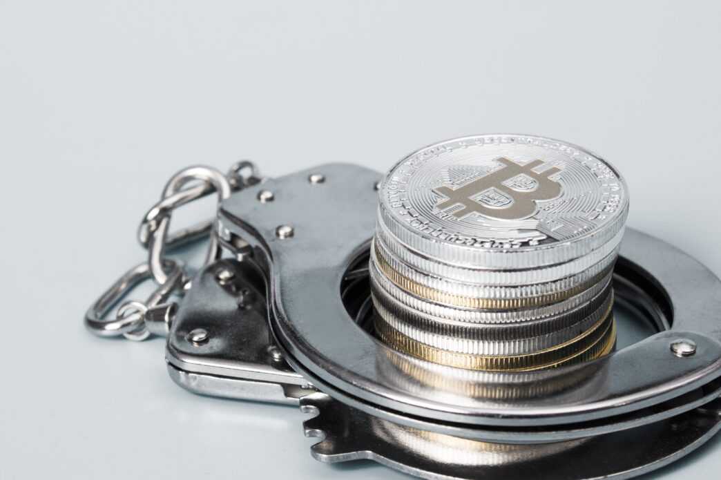 A stack of silver and gold Bitcoin coins resting on a pair of metal handcuffs.