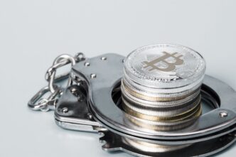 A stack of silver and gold Bitcoin coins resting on a pair of metal handcuffs.