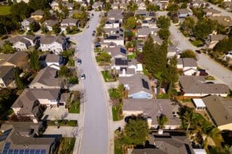 High aerial view of a dense suburban neighborhood with houses, solar panels, and curved streets.