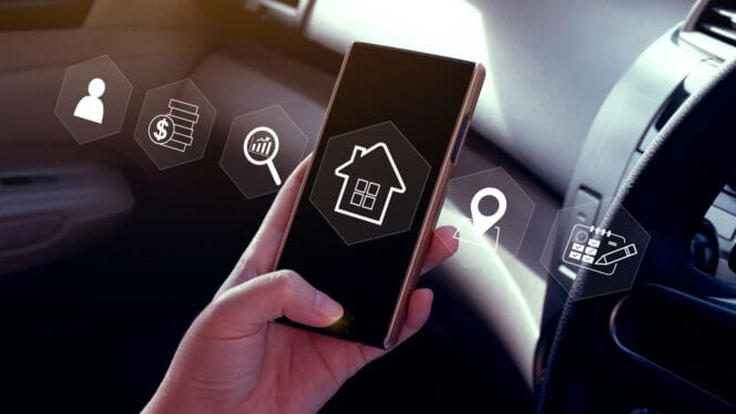 Hand holding a smartphone displaying a house icon, surrounded by holographic icons for people, money, search, and map, set inside a car.