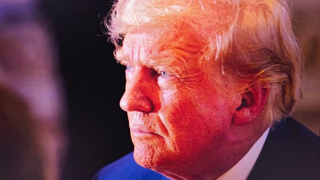 Close-up, profile image of Donald Trump with a serious expression, viewed through a digital screen grid.