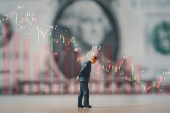 Miniature businessman looking down in front of a falling stock market graph and a blurred dollar bill.