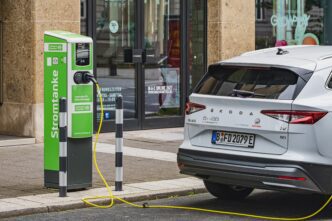 A white Skoda Enyaq iV is charging at a green and white "Stromtanke" electric vehicle charging station on a city street.