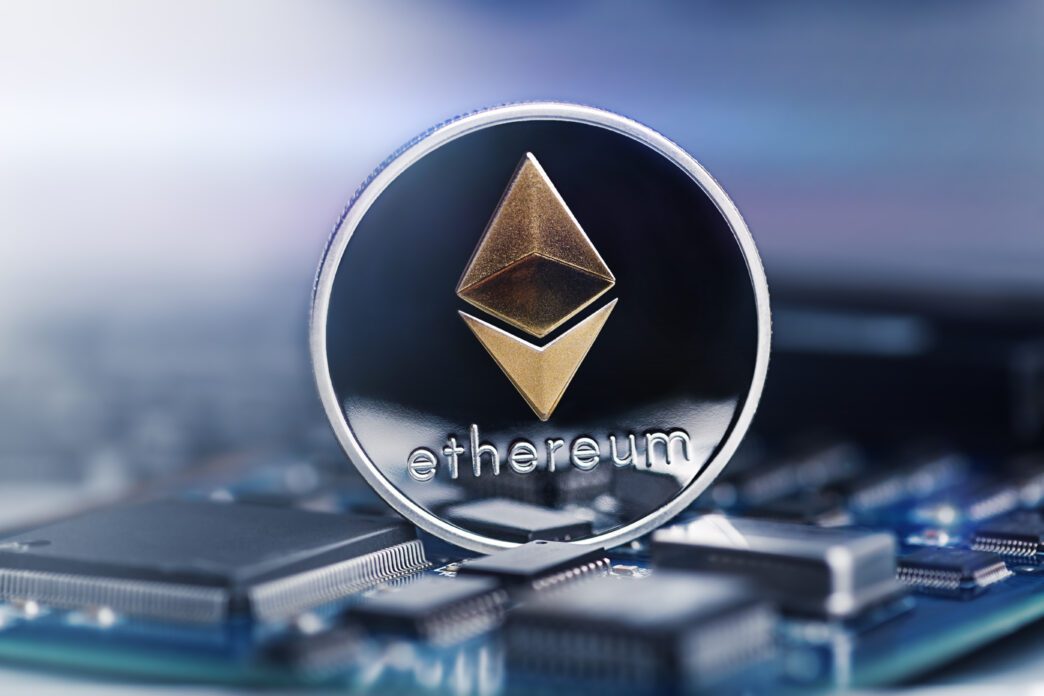 A physical Ethereum cryptocurrency coin with a gold symbol resting directly on a computer circuit board.