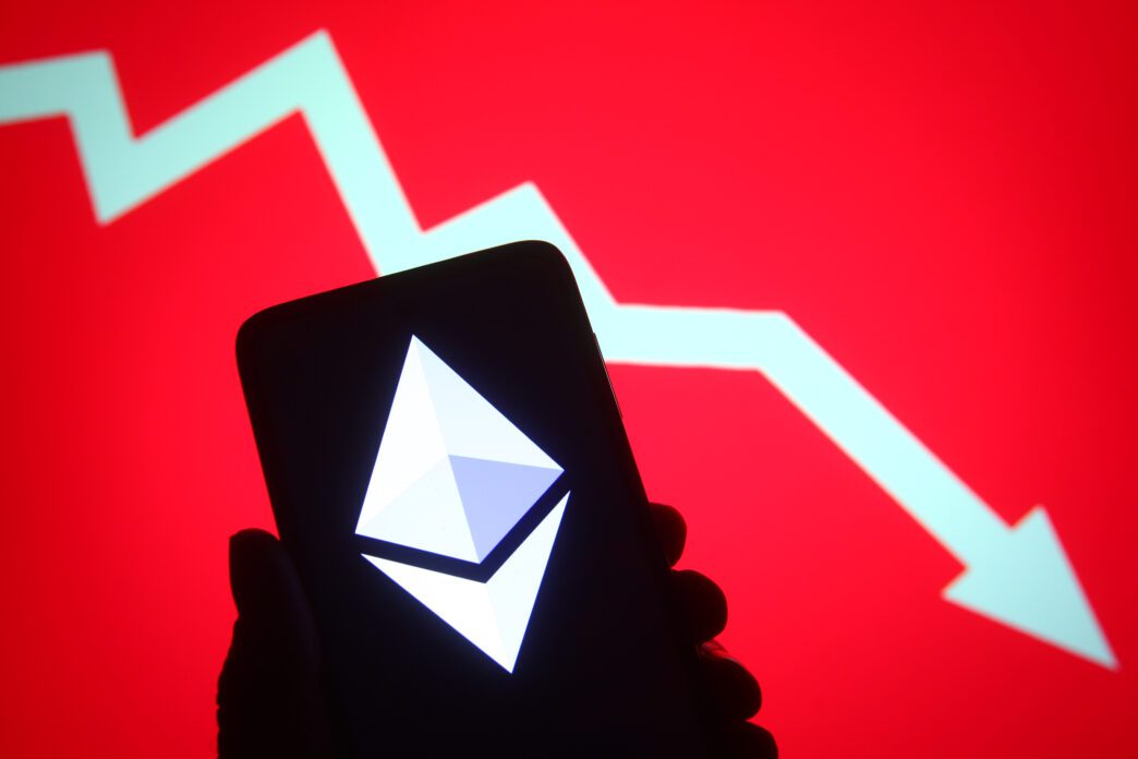 Ethereum logo on a phone screen silhouetted against a red background with a large downward arrow.