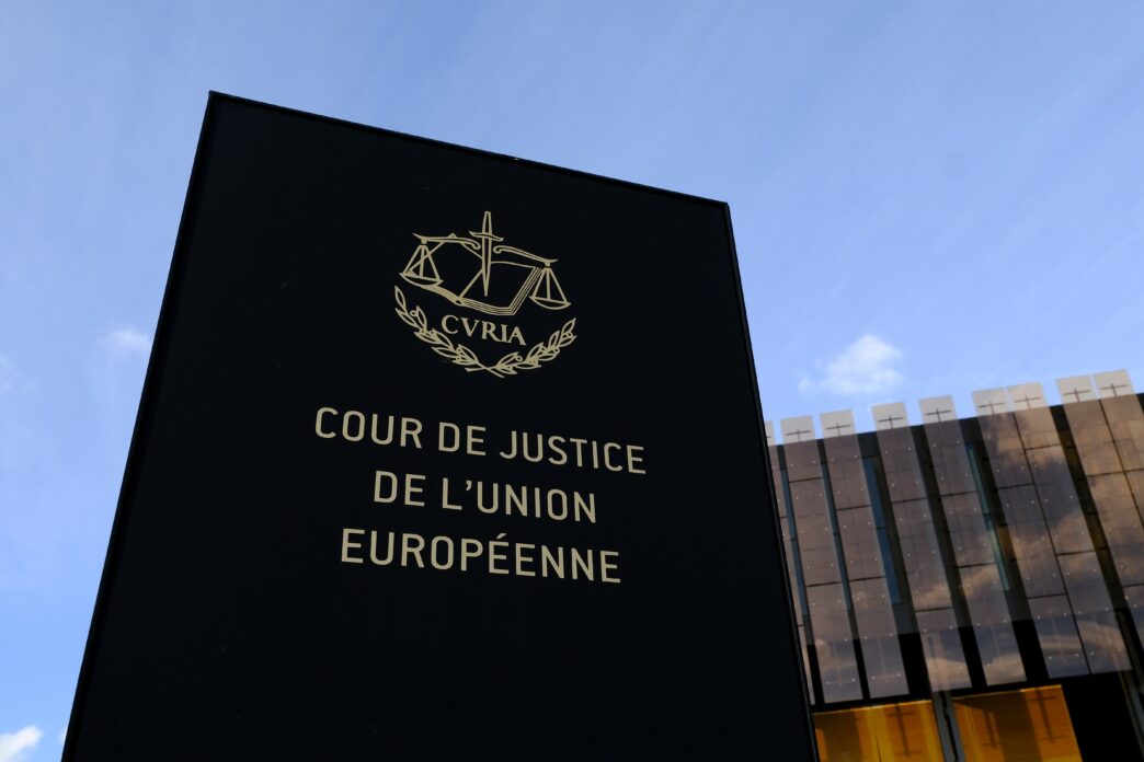 Sign for the European Court of Justice with the Curia logo, set against the building and blue sky.