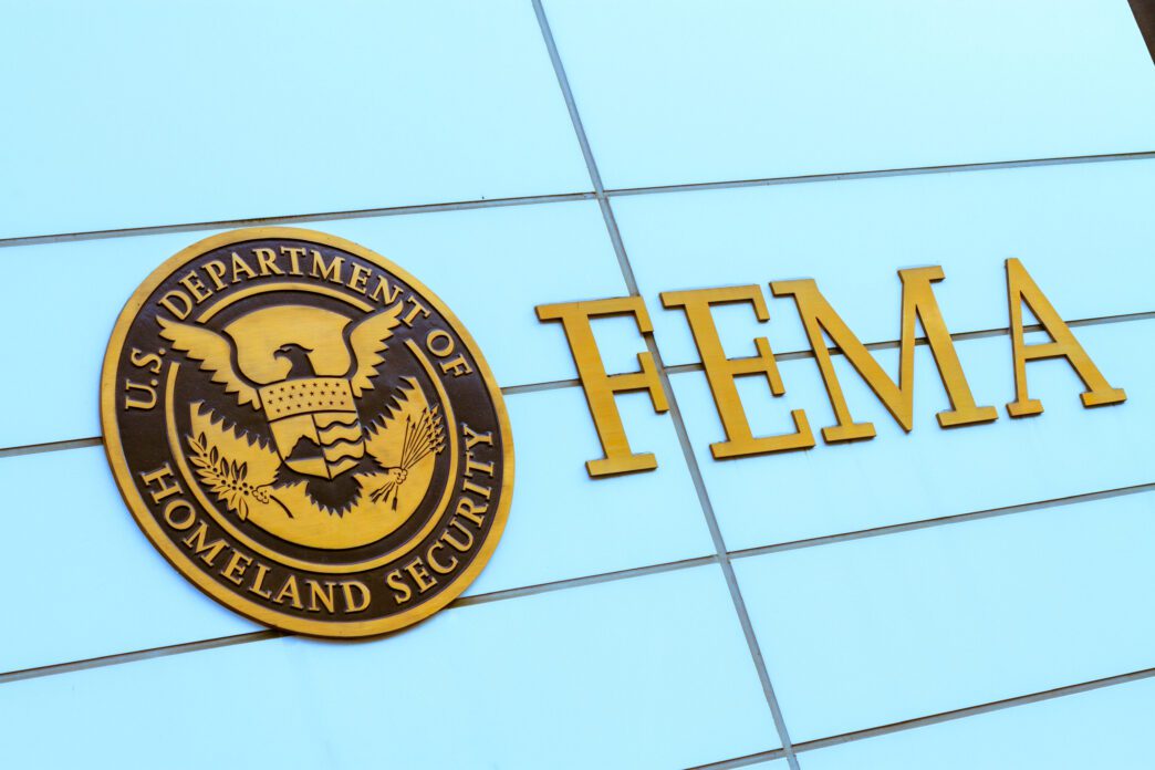 The gold FEMA logo and seal of the U.S. Department of Homeland Security on a blue glass building.