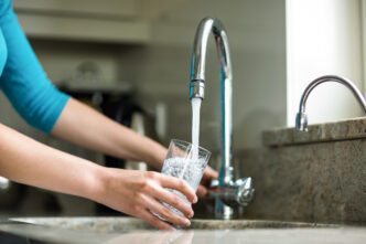 Close-up of hands filling a clear drinking glass with tap water from a modern kitchen faucet.