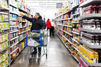 Man pushing a cart and reaching for a product in a brightly lit grocery aisle at Walmart.