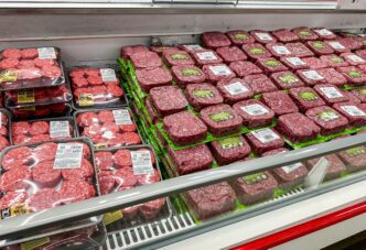 Fully stocked refrigerated display case filled with rows of packaged raw ground beef patties.