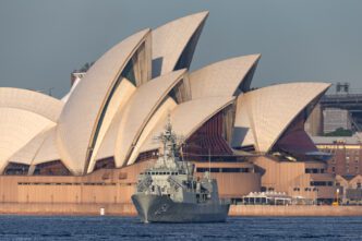 The HMAS Parramatta frigate sails in Sydney Harbour with the iconic shell-like roofs of the Sydney Opera House visible in the background.
