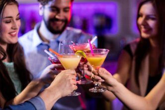 Group of friends happily toasting with colorful cocktails at a brightly lit bar.