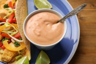 Close-up of a bowl of creamy pink sauce and a fish taco on a blue plate with lime wedges.