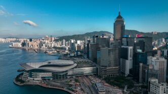 Aerial view of the modern Hong Kong skyline, Victoria Harbour, and mountains.