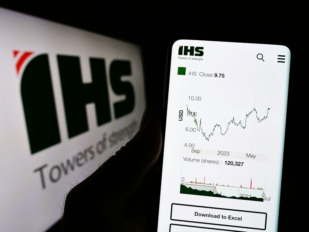 Hand holding a phone displaying the IHS Holding stock chart and closing price of 9.75.