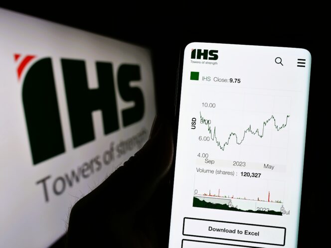 Hand holding a phone displaying the IHS Holding stock chart and closing price of 9.75.