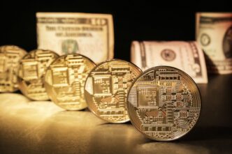 Five gold cryptocurrency coins with circuit board designs standing next to rolled US dollar bills.